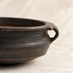 Black ceramic pot with a handle on a beige background