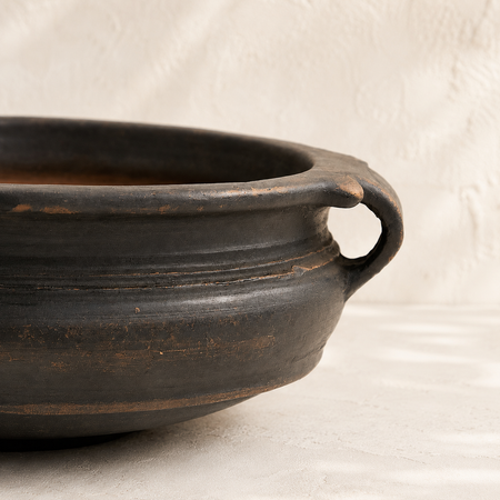 Black ceramic pot with a handle on a beige background