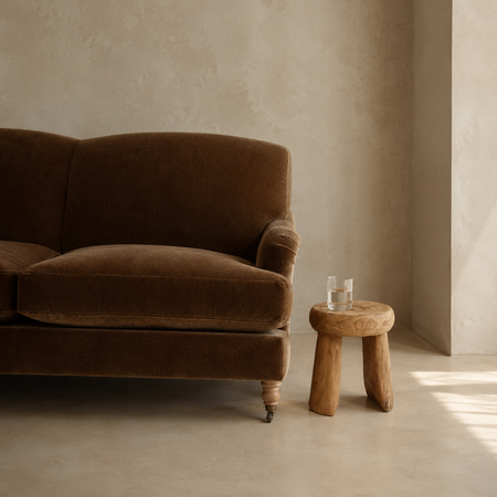 Brown sofa in a room with a wooden stool and glass of water.