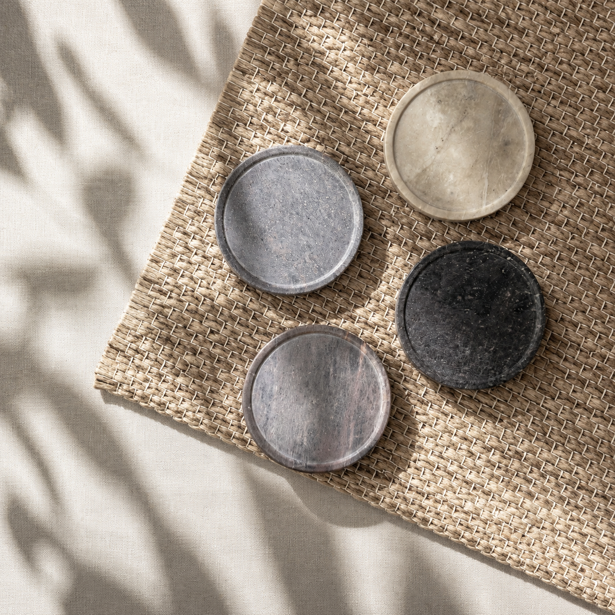 Four round stone coasters in gray and black on a woven mat with natural light casting shadows.