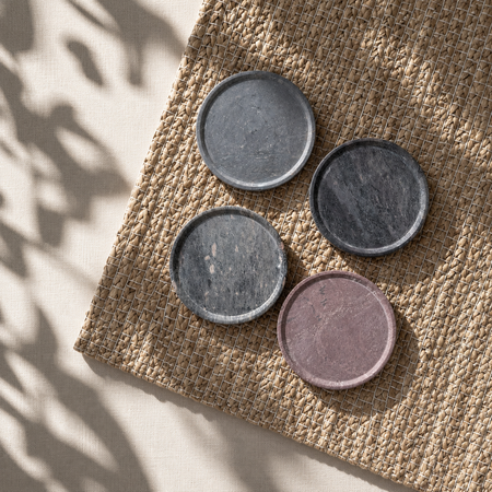 Four round ceramic coasters in gray and purple on a textured woven surface.