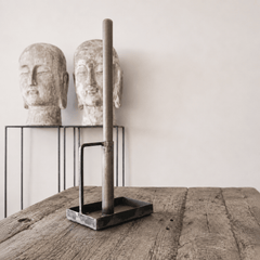 Decorative candlestick on a wooden surface, with stone head sculptures in the background.
