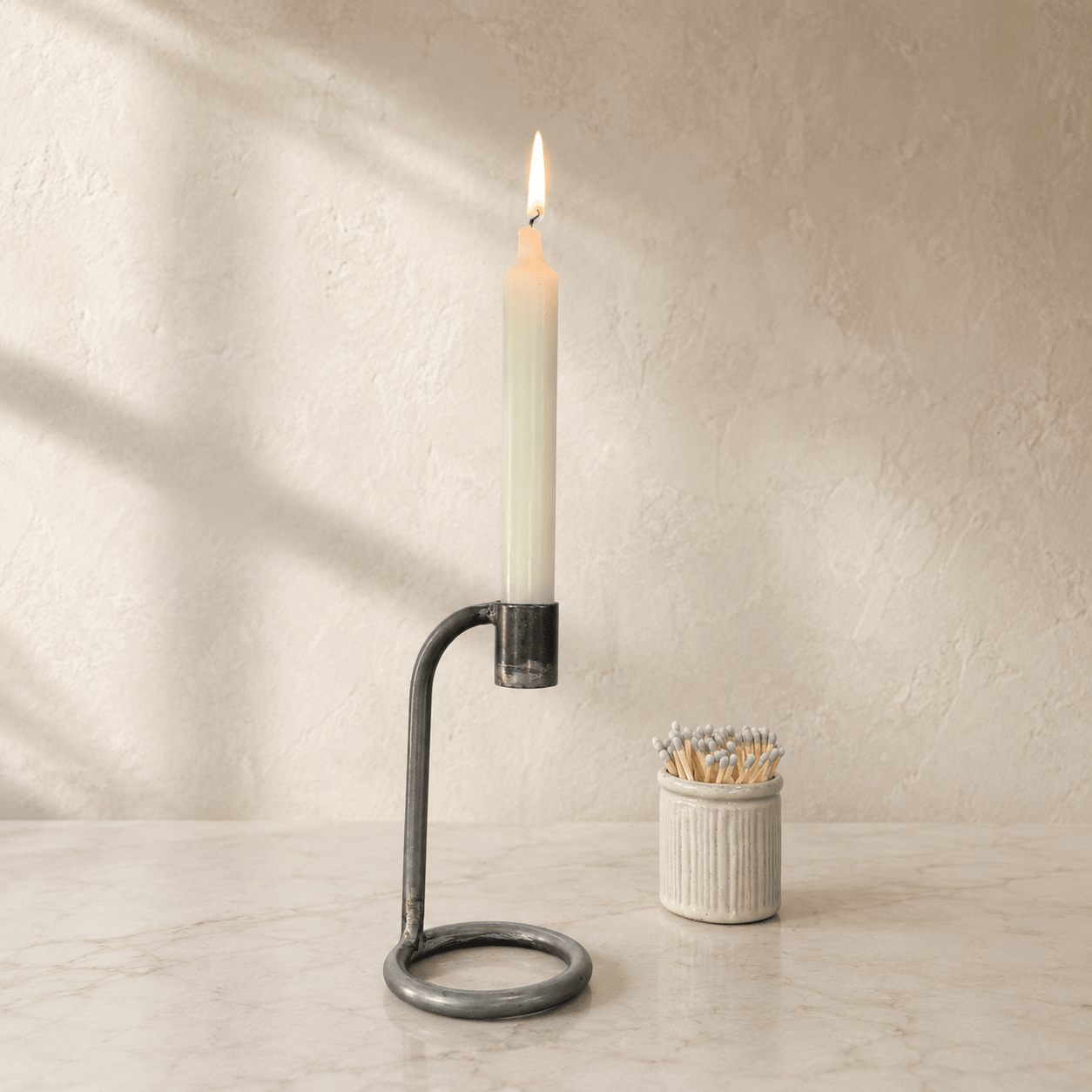 Candle in a holder with matches on a marble surface and beige wall background