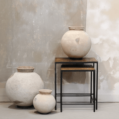 Three rustic cream-colored ceramic vases of varying sizes styled on and next to a two-tier wooden nesting side table with black metal frames, set against a textured plaster wall.
