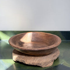 A round wooden bowl with a rustic handcrafted look, resting on a matching thick wooden base against a split white and green background.