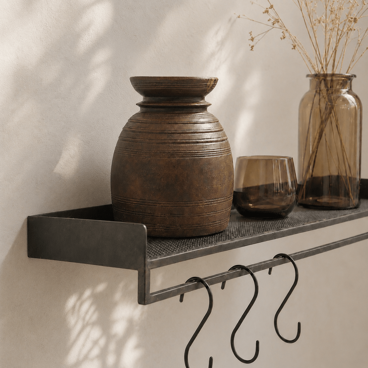 Decorative shelf with a large brown vase, glass, and jar against a neutral wall.