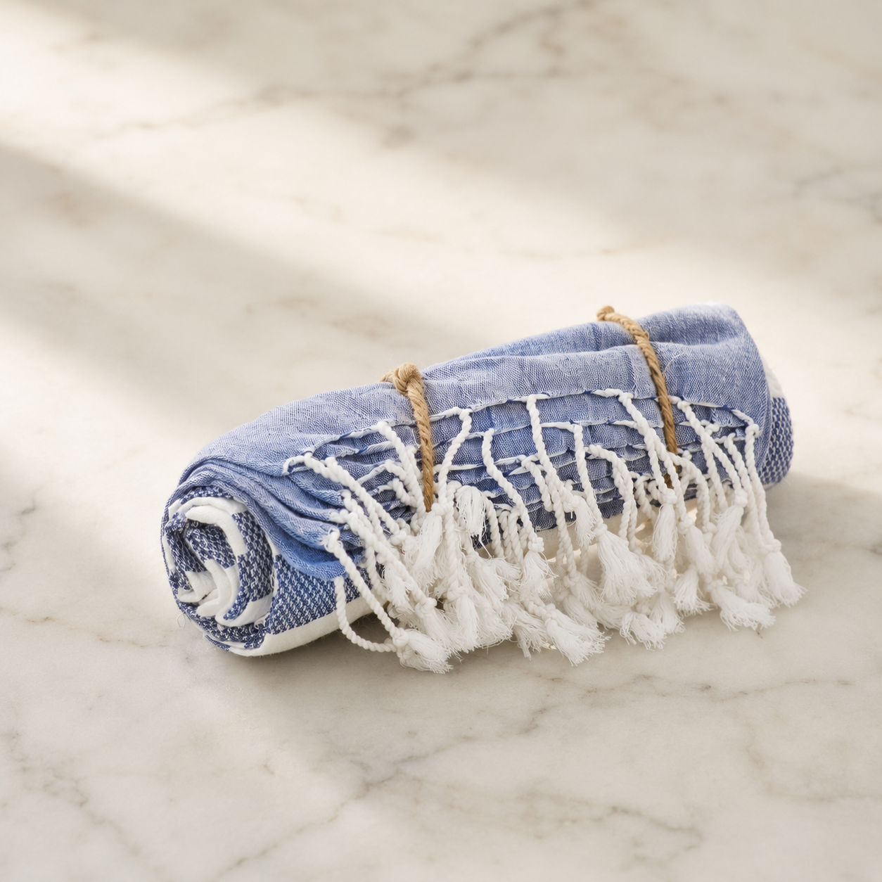 Rolled-up blue towel with white fringe on a marble surface