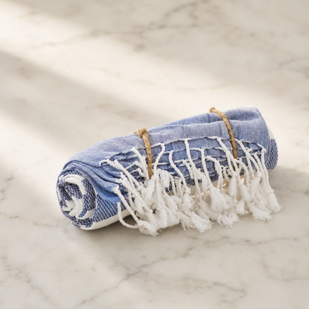 Rolled-up blue towel with white fringe on a marble surface