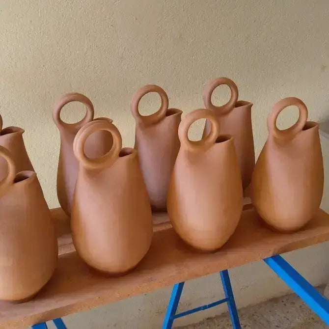 Row of terracotta vases with circular handles on a wooden table.