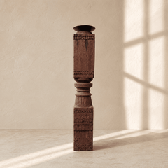 Decorative wooden column against a beige wall with sunlight casting shadows.