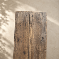 Rustic wooden plank against a beige wall with shadow patterns