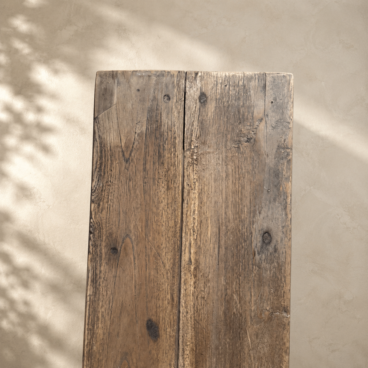 Rustic wooden plank against a beige wall with shadow patterns