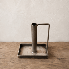 Metal candlestick holder with handle on a square base on a wooden surface