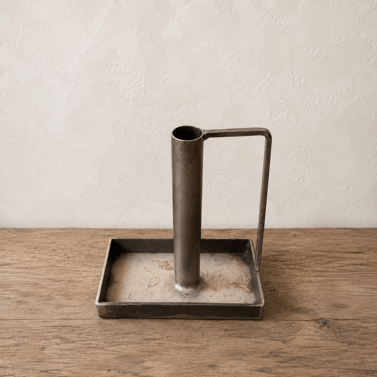 Metal candlestick holder with handle on a square base on a wooden surface