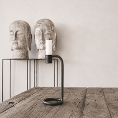 Candle holder with a candle between two stone Buddha heads on a wooden surface.