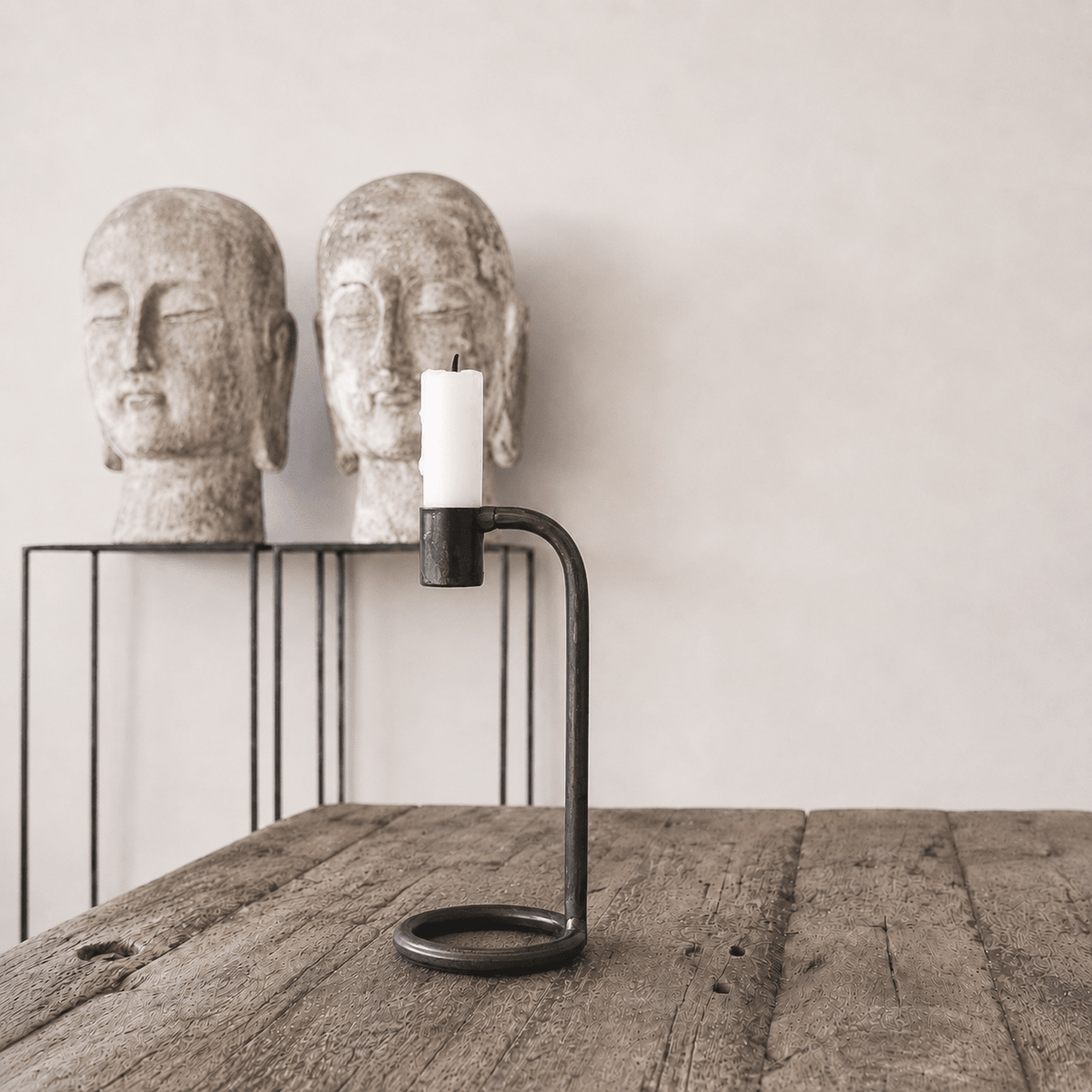 Candle holder with a candle between two stone Buddha heads on a wooden surface.