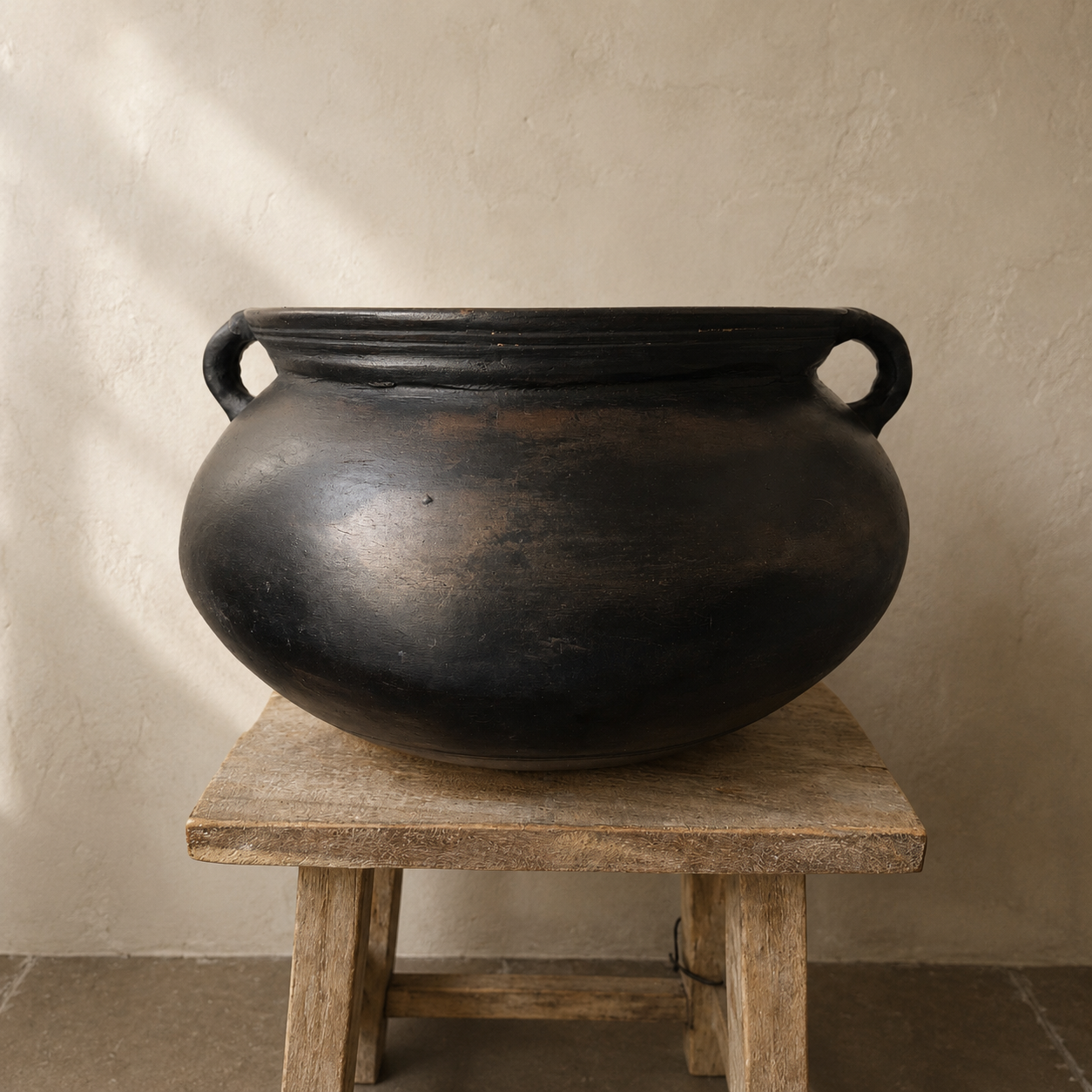 Black pot with handles on a wooden stool against a beige wall
