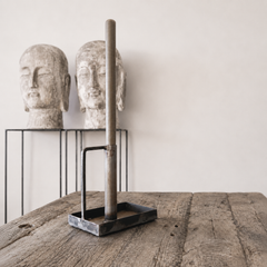 Tall candlestick with stone heads on a wooden surface.