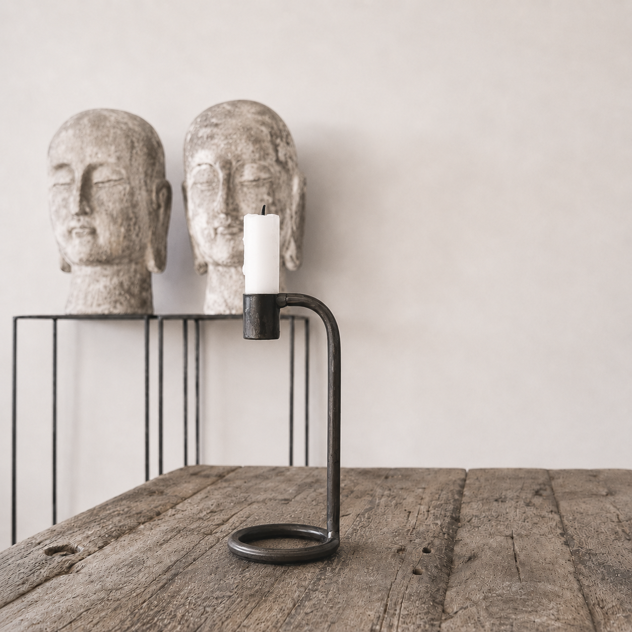 Candle holder with a candle between two stone Buddha heads on a wooden surface.