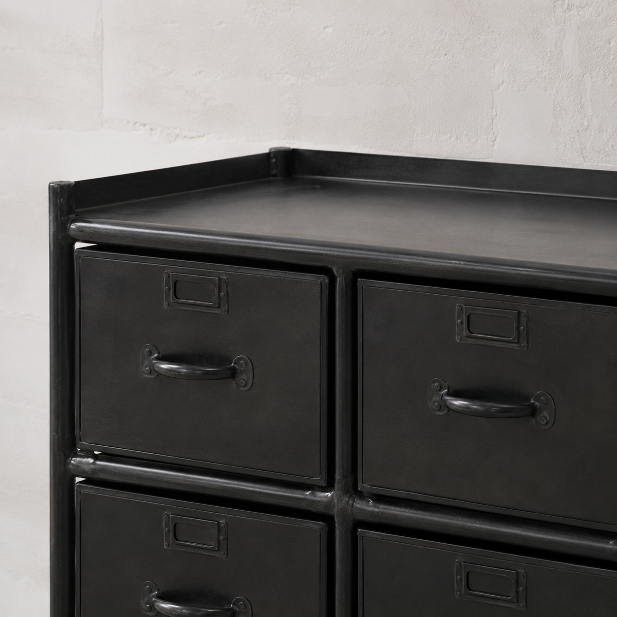 Black metal dresser with multiple drawers against a light gray wall.