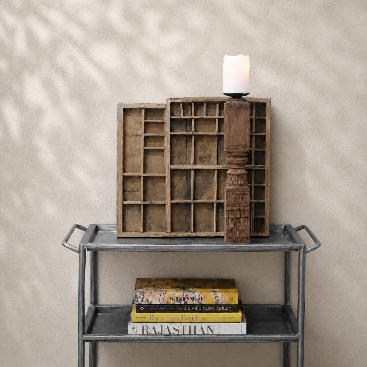 Decorative wooden shelf with books and a wooden candle stick on a metal table against a beige wall.