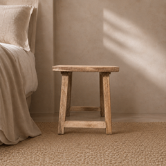 Wooden stool against a beige wall in a bedroom setting