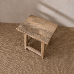 Wooden stool on a textured brown floor with a neutral wall background
