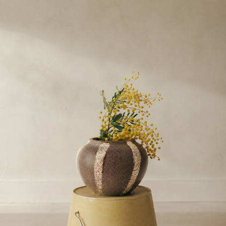 Decorative vase with yellow flowers on a yellow bucket against a neutral background
