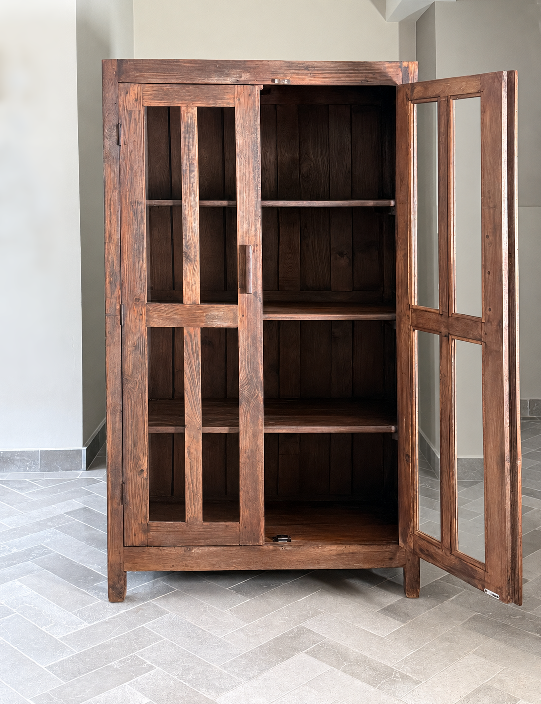 Wooden cabinet with glass doors on a gray tiled floor.