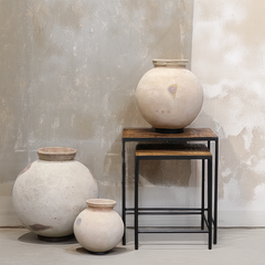 Three rustic ceramic vases in varying sizes styled on and next to a two-tier wooden and metal side table against a textured plaster wall.