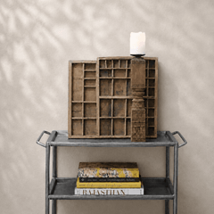 Decorative wooden shelf with books and a candle on a metal table against a beige wall.