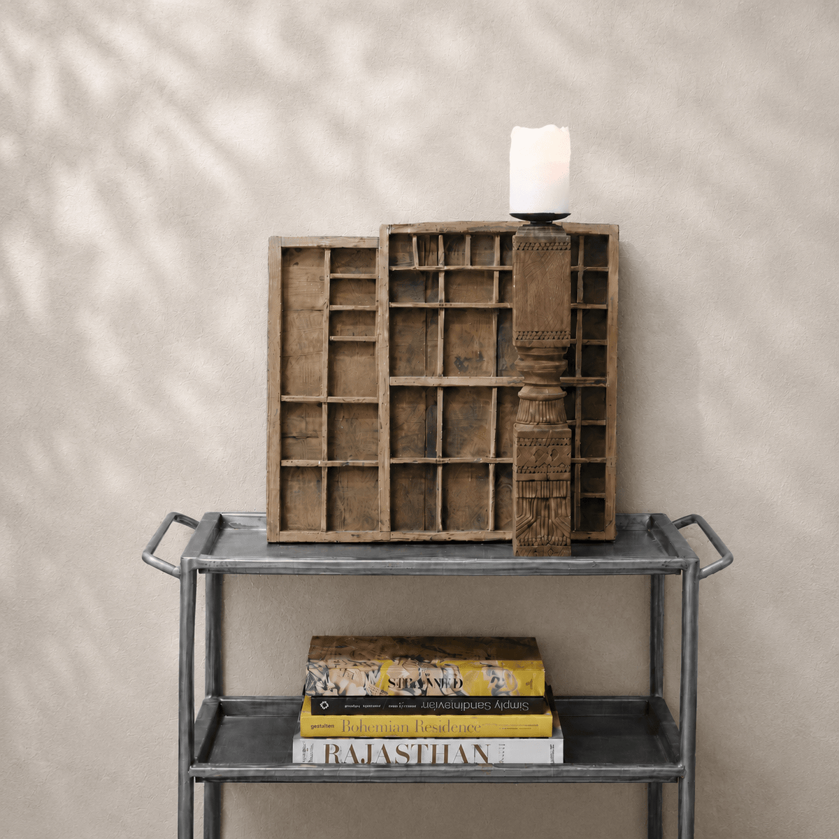 Decorative wooden shelf with books and a candle on a metal table against a beige wall.