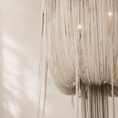 Close-up of a modern chandelier with beige leather ribbons against a neutral background