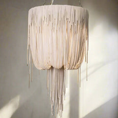 A lether pendant chandelier with a textured, frayed fringe design in a warm cream or off-white color, hanging against a neutral wall with soft shadows.